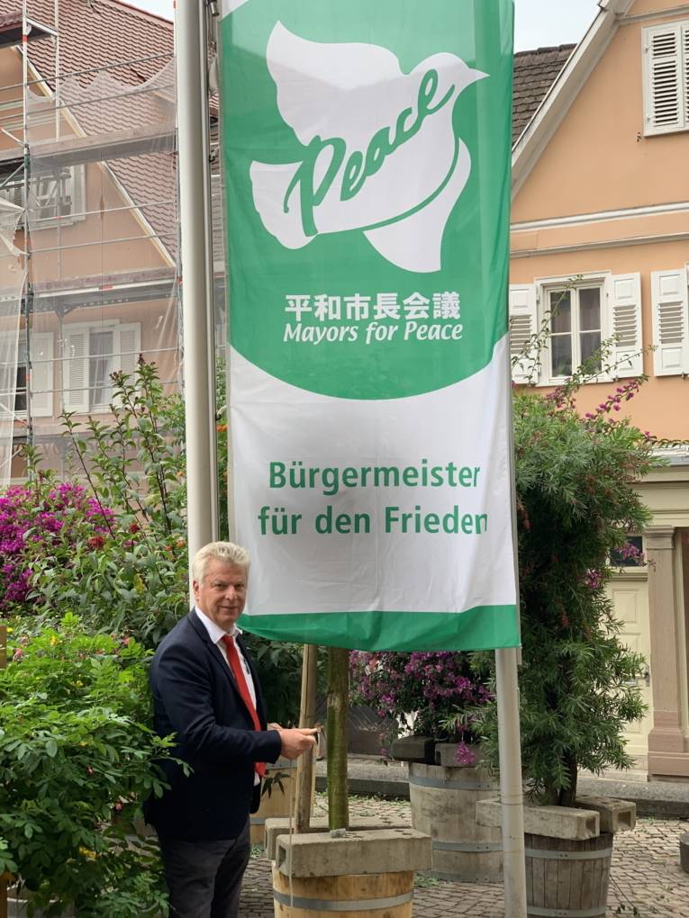 Ein Mann im Anzug hisst die weiß-grüne Mayors-for-Peace-Flagge in Bietigheim-Bissingen (Baden-Württemberg)